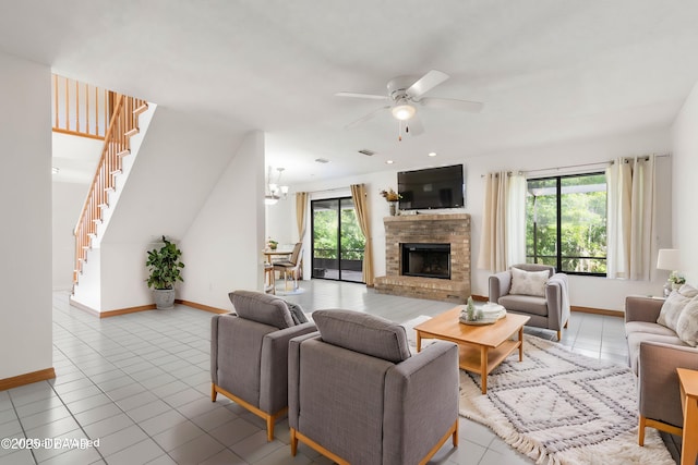 tiled living room with stairway, a brick fireplace, ceiling fan with notable chandelier, and a healthy amount of sunlight