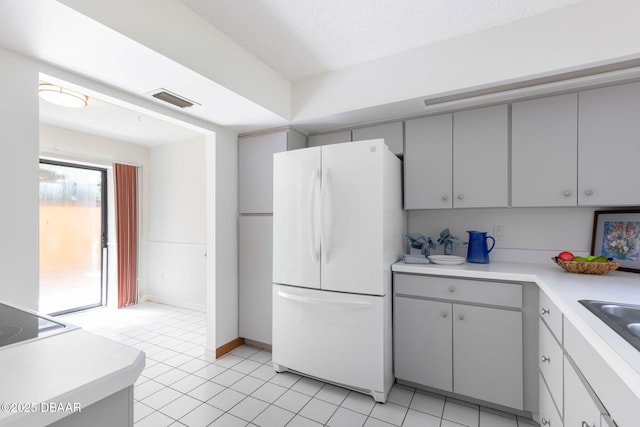 kitchen featuring freestanding refrigerator, light tile patterned floors, a textured ceiling, visible vents, and light countertops