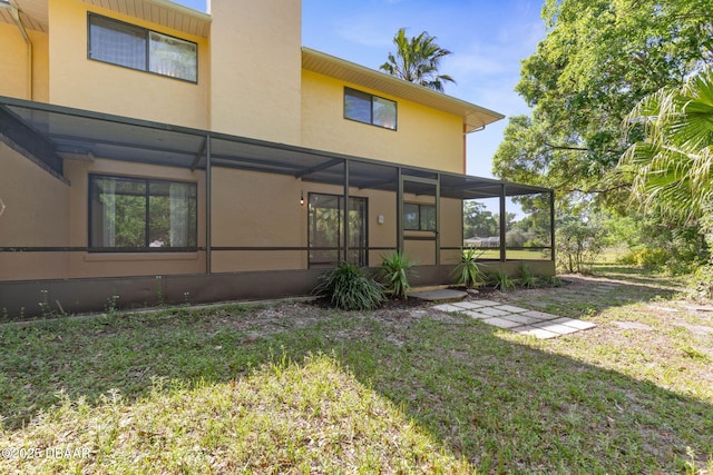 rear view of property with a sunroom, a yard, stucco siding, and a chimney