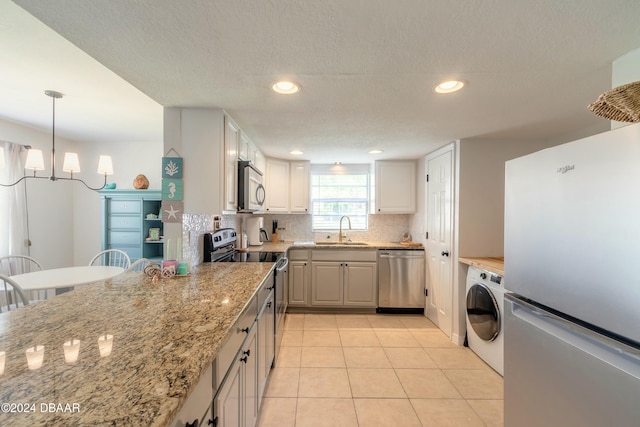 kitchen featuring white cabinetry, sink, hanging light fixtures, stainless steel appliances, and washer / clothes dryer