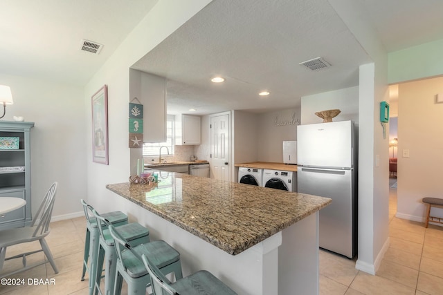 kitchen featuring appliances with stainless steel finishes, tasteful backsplash, stone countertops, light tile patterned flooring, and kitchen peninsula