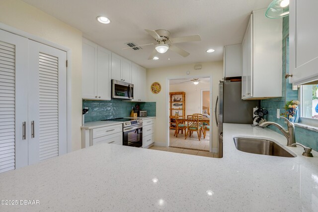 kitchen with visible vents, appliances with stainless steel finishes, white cabinets, a sink, and light stone countertops