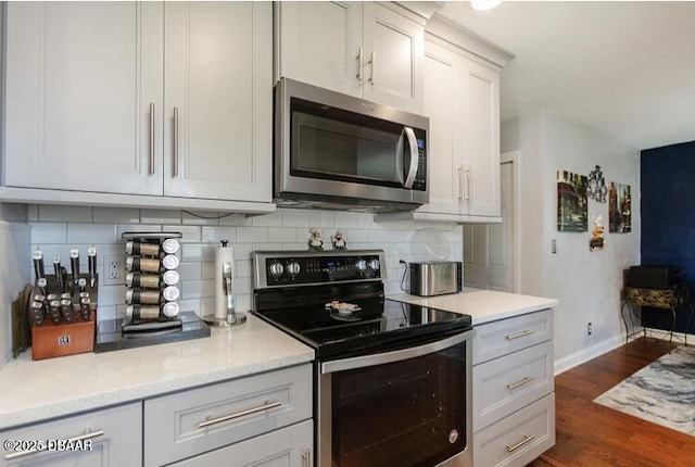 kitchen featuring baseboards, appliances with stainless steel finishes, dark wood-type flooring, light countertops, and backsplash