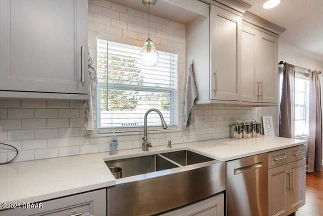 kitchen featuring decorative backsplash, hanging light fixtures, light countertops, stainless steel dishwasher, and a sink