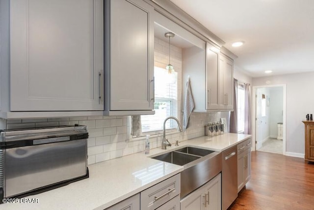 kitchen with dishwasher, backsplash, light wood-type flooring, pendant lighting, and a sink