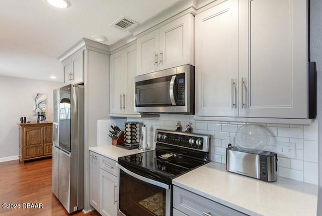 kitchen featuring appliances with stainless steel finishes, light countertops, visible vents, and wood finished floors