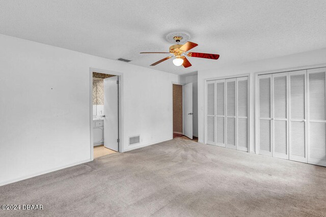 unfurnished bedroom with a textured ceiling, ensuite bath, ceiling fan, and two closets