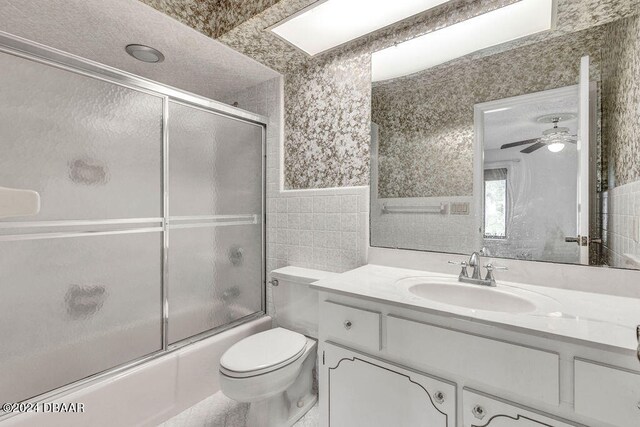 full bathroom featuring tile walls, shower / bath combination with glass door, vanity, toilet, and ceiling fan