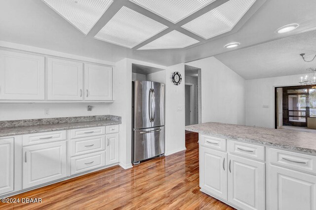 kitchen featuring white cabinets, light hardwood / wood-style flooring, a notable chandelier, and stainless steel refrigerator