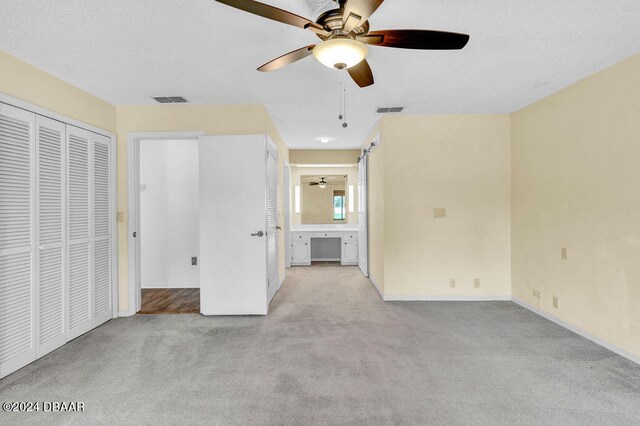 unfurnished bedroom featuring a textured ceiling, light colored carpet, ceiling fan, and connected bathroom