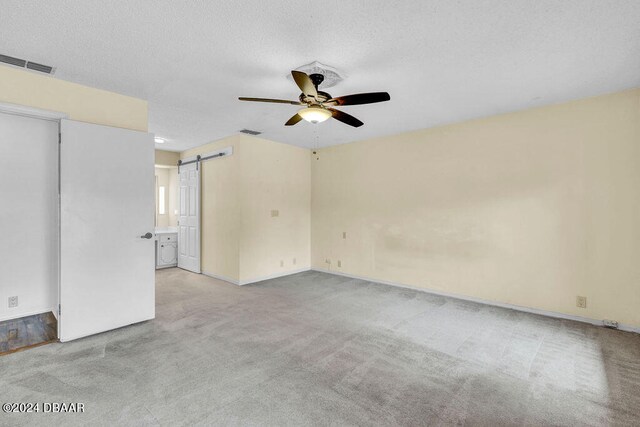 carpeted empty room featuring a textured ceiling, a barn door, and ceiling fan