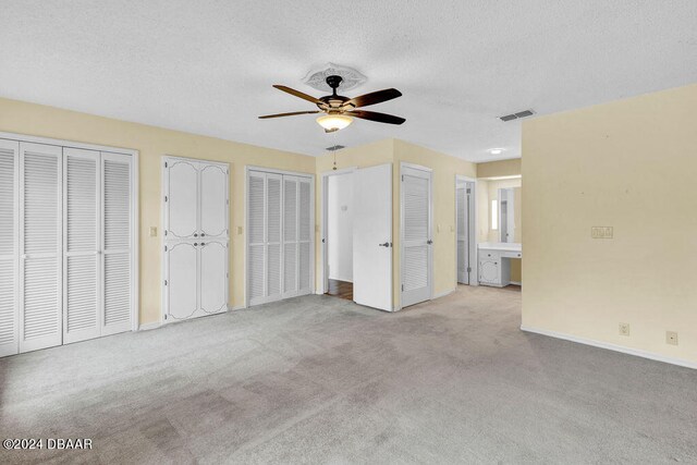 unfurnished bedroom with connected bathroom, a textured ceiling, light carpet, two closets, and ceiling fan