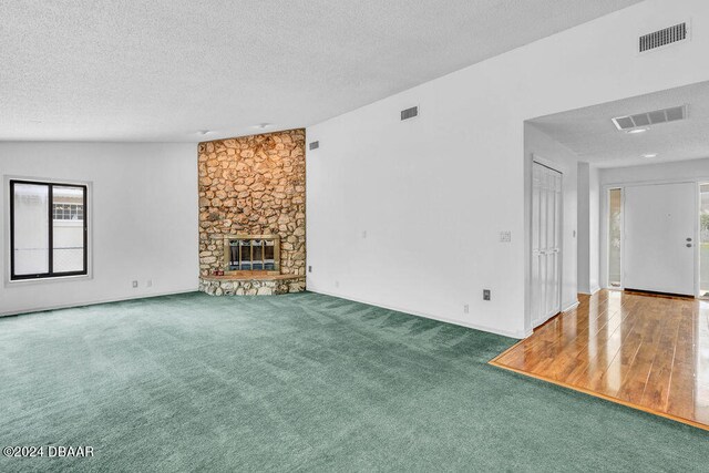 unfurnished living room with a textured ceiling, lofted ceiling, hardwood / wood-style floors, and a fireplace