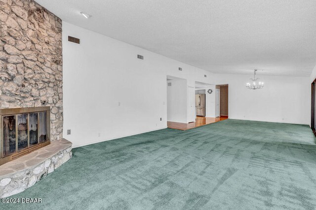 unfurnished living room featuring a stone fireplace, a textured ceiling, an inviting chandelier, and carpet