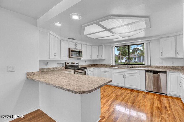 kitchen with stainless steel appliances, white cabinetry, light wood-type flooring, and kitchen peninsula