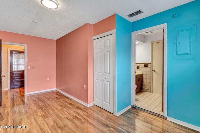 unfurnished bedroom featuring electric panel, light hardwood / wood-style flooring, a textured ceiling, and a closet