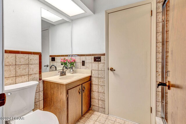 bathroom with toilet, vanity, tile walls, and tile patterned floors