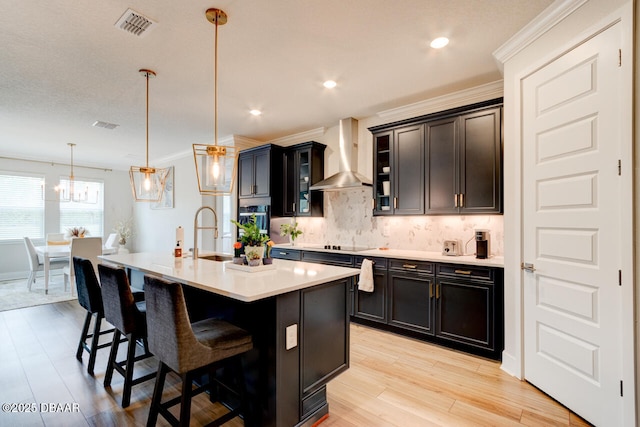 kitchen featuring a breakfast bar area, a sink, light countertops, wall chimney range hood, and backsplash