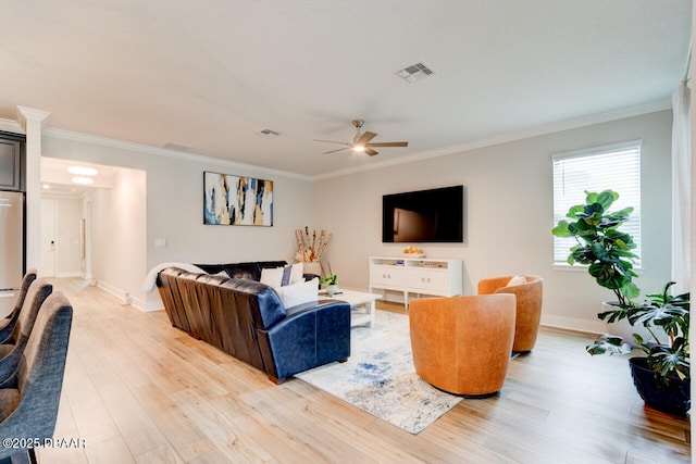 living room with ornamental molding, light wood-type flooring, visible vents, and baseboards