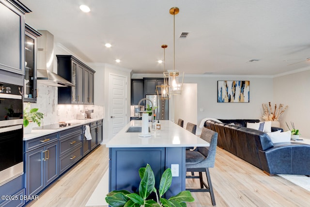 kitchen with visible vents, wall chimney exhaust hood, appliances with stainless steel finishes, open floor plan, and a sink