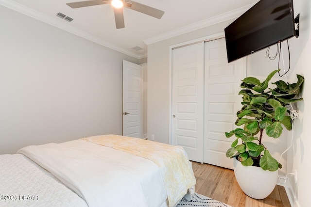 bedroom featuring light wood-style flooring, visible vents, a ceiling fan, ornamental molding, and a closet