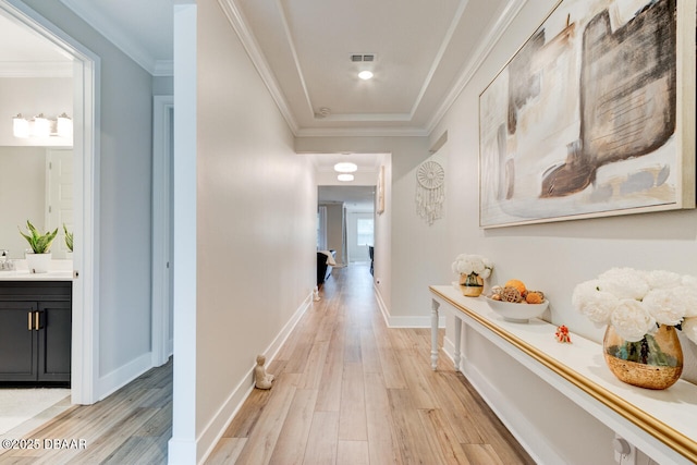 hall with light wood-style floors, visible vents, ornamental molding, and baseboards