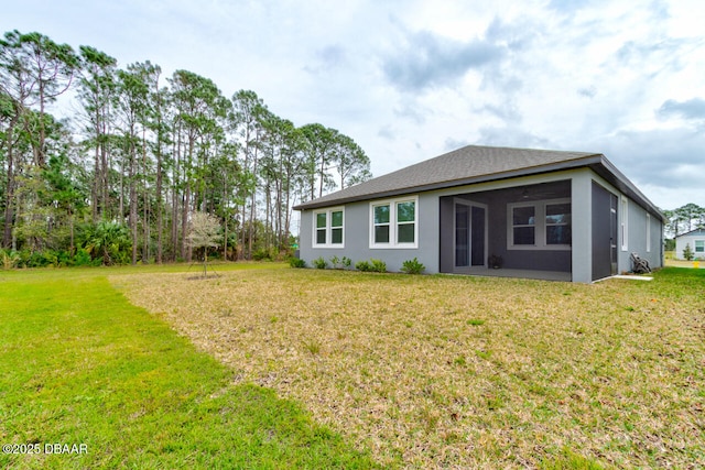 rear view of property featuring a sunroom, a lawn, and stucco siding