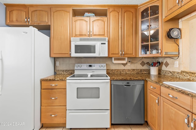 kitchen with decorative backsplash, white appliances, light tile patterned floors, and dark stone counters