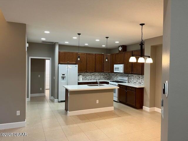 kitchen featuring sink, hanging light fixtures, white appliances, a kitchen island with sink, and decorative backsplash