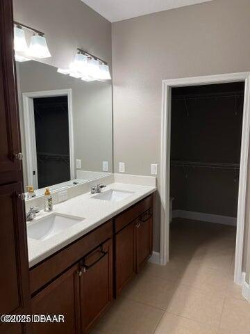 full bathroom with a sink, a spacious closet, baseboards, and double vanity