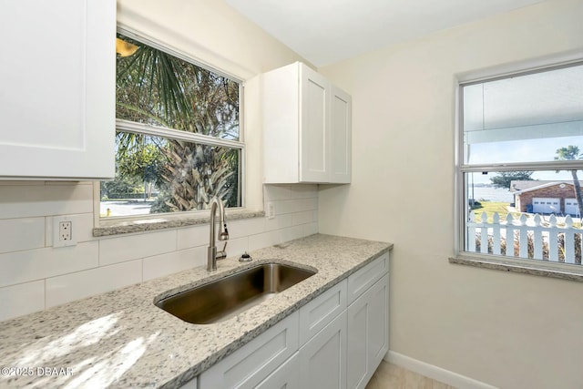 kitchen with light stone counters, backsplash, sink, and white cabinets