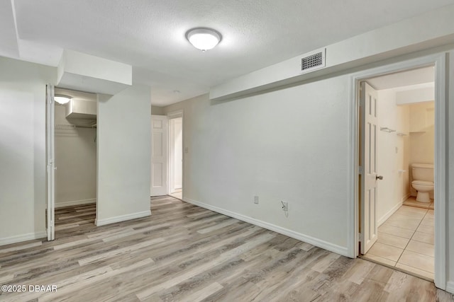 unfurnished bedroom with connected bathroom, light hardwood / wood-style flooring, a closet, and a textured ceiling