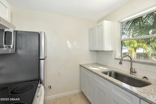 kitchen featuring light stone countertops, sink, decorative backsplash, and white cabinets