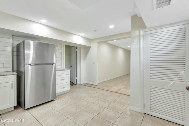 kitchen with light tile patterned flooring, light stone countertops, white cabinets, and stainless steel refrigerator