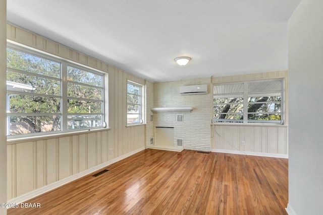 unfurnished living room featuring hardwood / wood-style flooring, a fireplace, and a wall unit AC