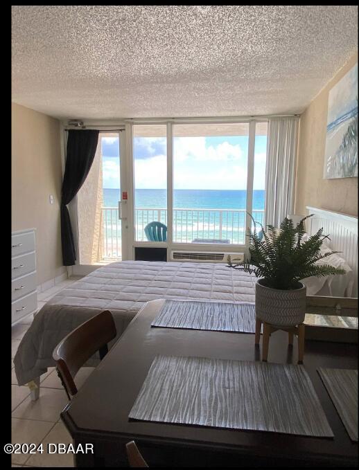 bedroom featuring tile patterned floors, access to exterior, a water view, and a textured ceiling