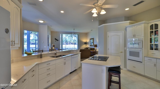 kitchen featuring a kitchen island, a kitchen bar, sink, white appliances, and white cabinetry