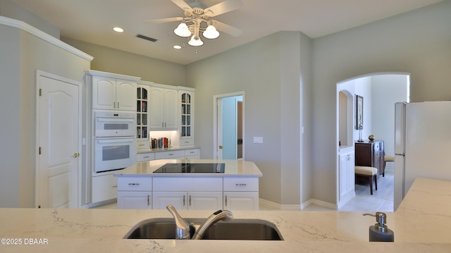 kitchen with white appliances, white cabinetry, ceiling fan, sink, and light stone counters