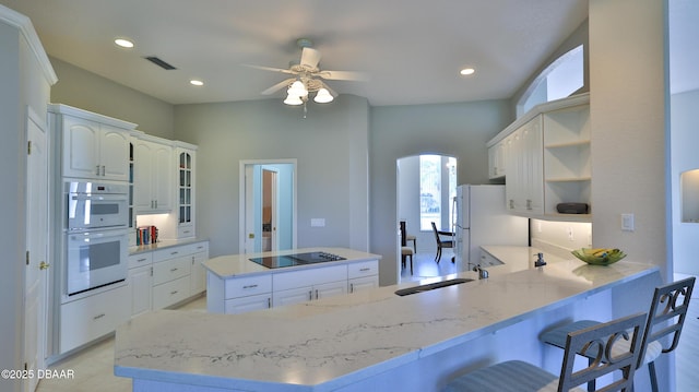 kitchen with white appliances, a kitchen bar, white cabinetry, sink, and kitchen peninsula