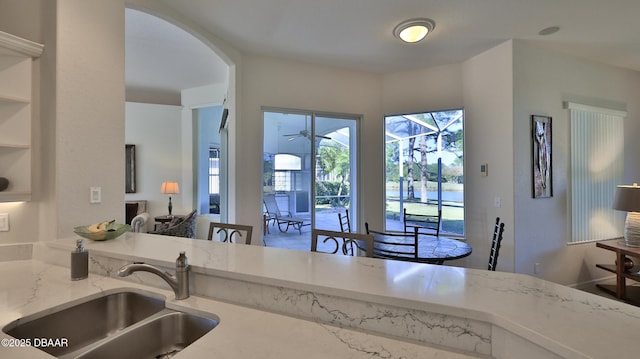 kitchen featuring light stone counters, sink, and ceiling fan