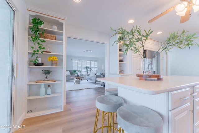 kitchen with white cabinetry, ceiling fan, light hardwood / wood-style flooring, a kitchen bar, and a kitchen island