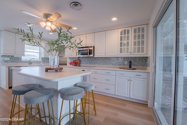 kitchen with light wood-type flooring, backsplash, stainless steel appliances, white cabinets, and a center island