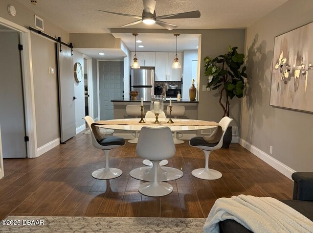 dining room featuring dark hardwood / wood-style floors, ceiling fan, a barn door, and a textured ceiling