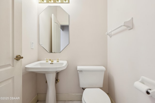half bathroom with toilet, baseboards, a sink, and tile patterned floors