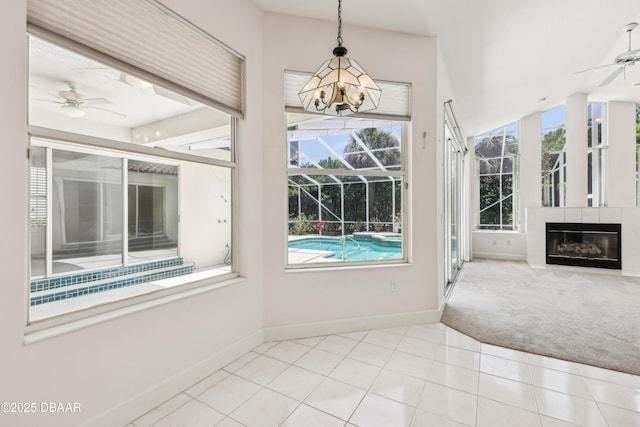 unfurnished dining area featuring baseboards, carpet, a glass covered fireplace, and ceiling fan with notable chandelier