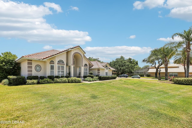 mediterranean / spanish home with a tiled roof, stucco siding, and a front lawn