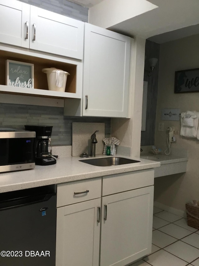 kitchen with white cabinetry, black dishwasher, light tile patterned floors, decorative backsplash, and sink