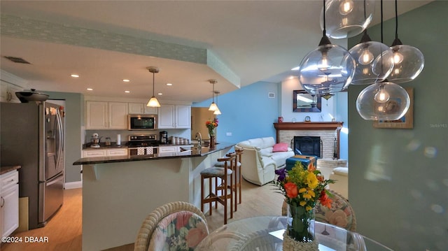 kitchen with pendant lighting, a kitchen breakfast bar, light hardwood / wood-style flooring, white cabinetry, and stainless steel appliances