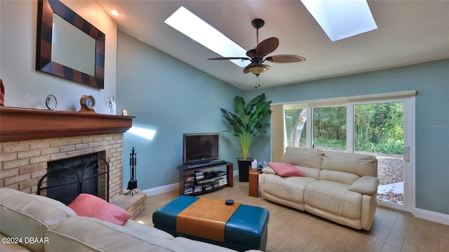 living room with a brick fireplace, light hardwood / wood-style floors, lofted ceiling with skylight, and ceiling fan