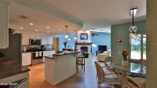 kitchen featuring white cabinetry, hanging light fixtures, a breakfast bar, appliances with stainless steel finishes, and light wood-type flooring